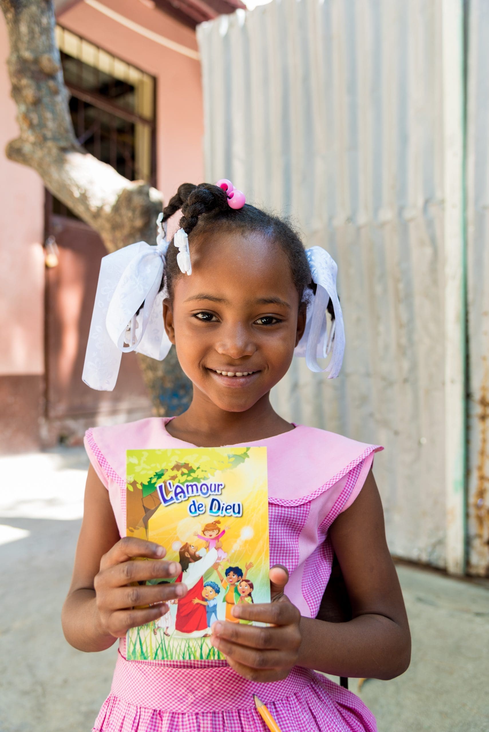 A smiling girl in a pink dress holding a children's Bible storybook in Haiti
